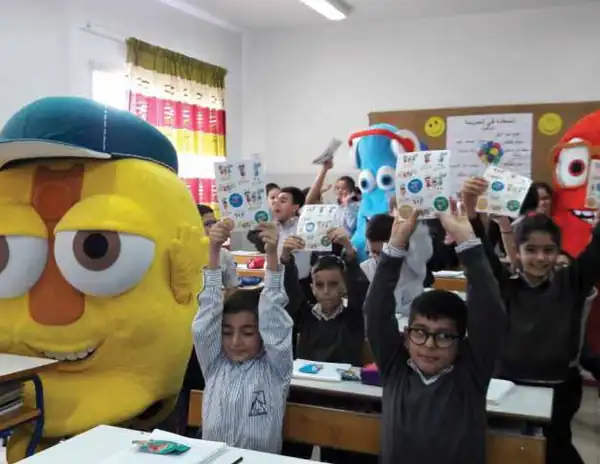 Children holding up leaflets beside mascots during a school visit
